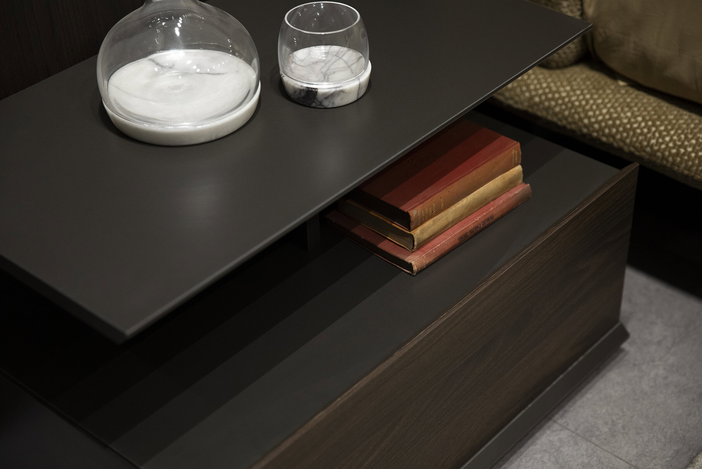 Sleek black coffee table with a modern design, featuring a smooth surface and open storage space with vintage books, decorated with glass vases for stylish home décor.