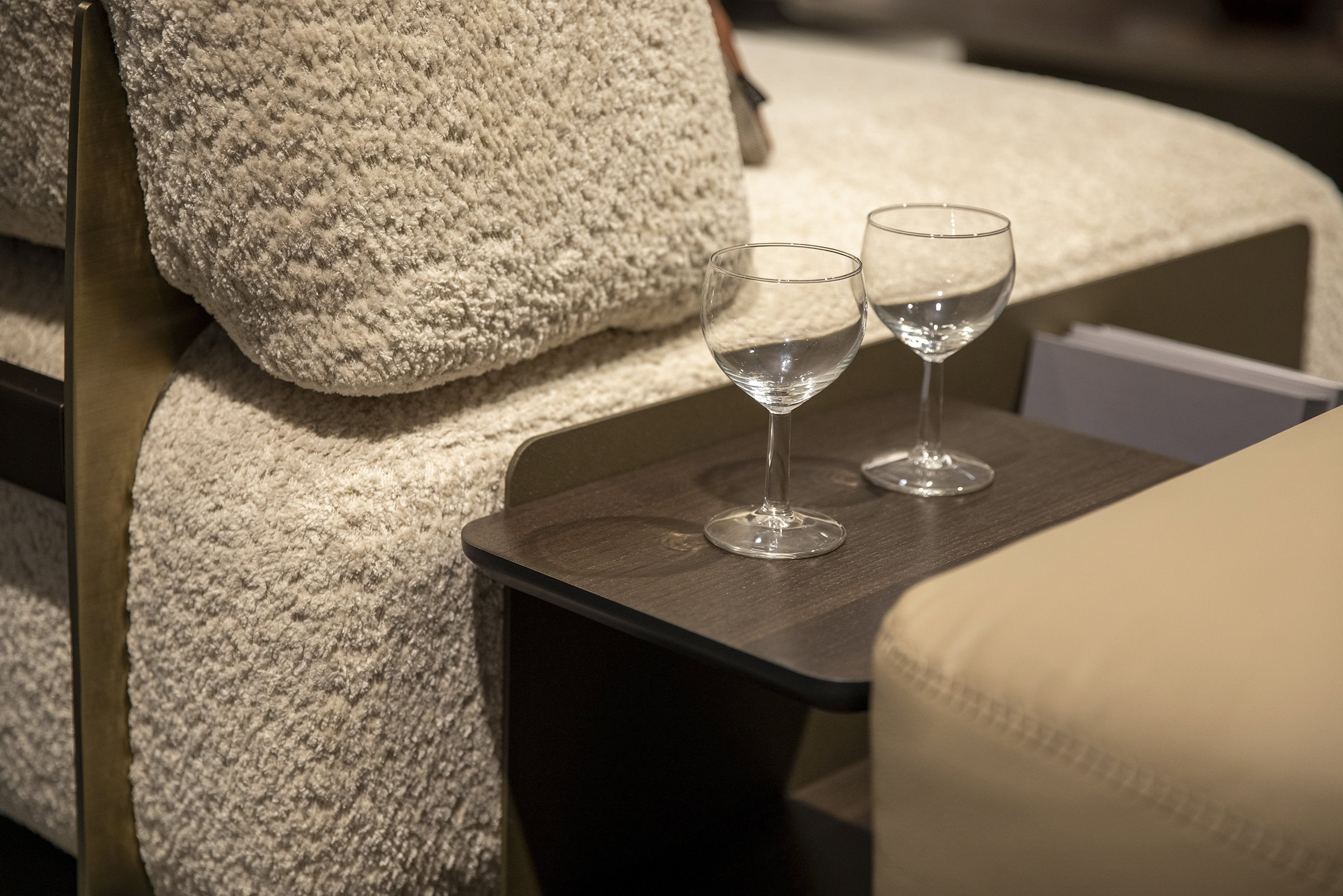 Luxurious beige textured sofa with brass accents and glassware on a dark wooden side table, emphasizing stylish modern furniture and home decor options at Saloni Furniture.