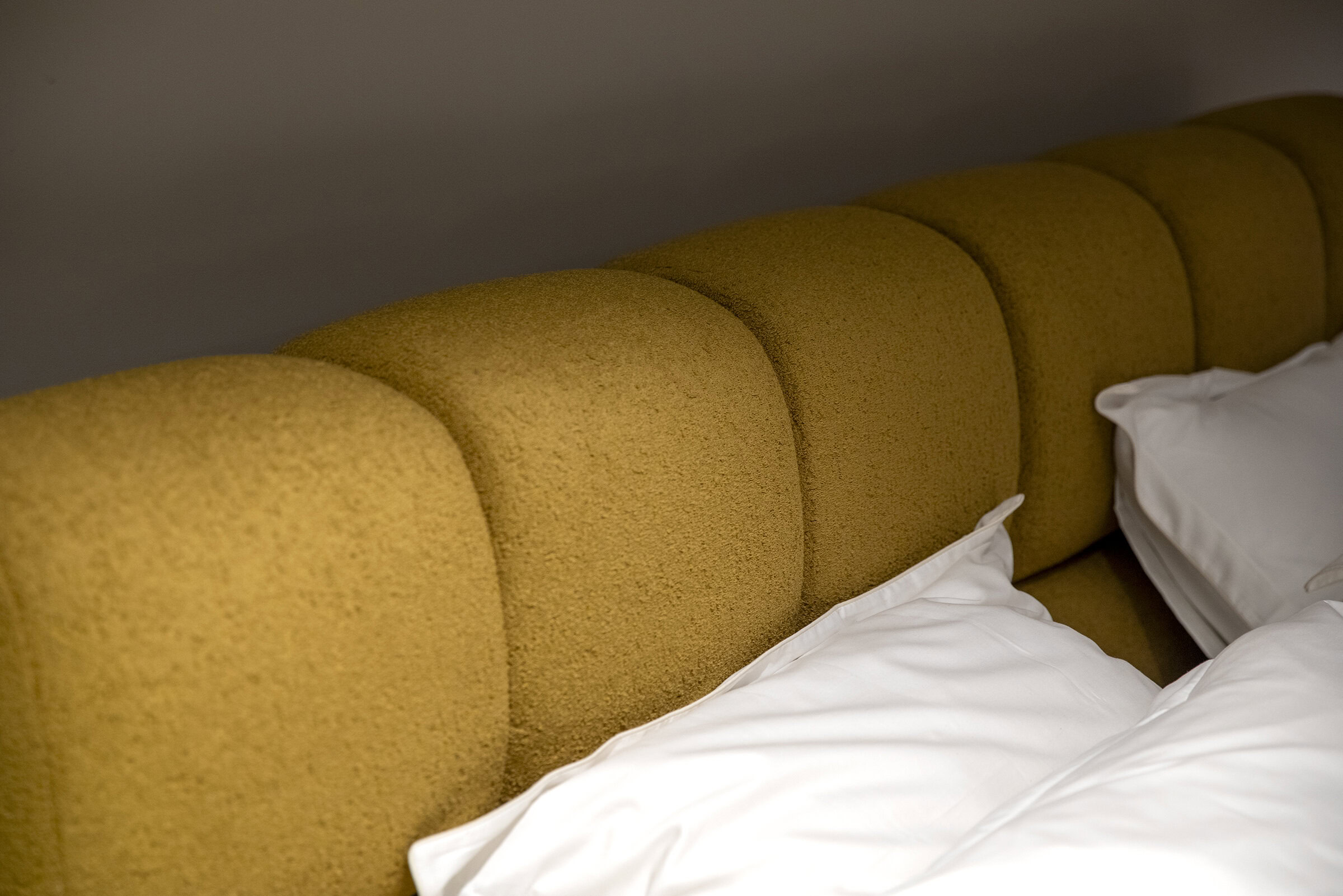 Modern mustard yellow upholstered bed headboard with white bedding and pillows, showcasing stylish bedroom furniture design for a cozy and elegant bedroom setting.