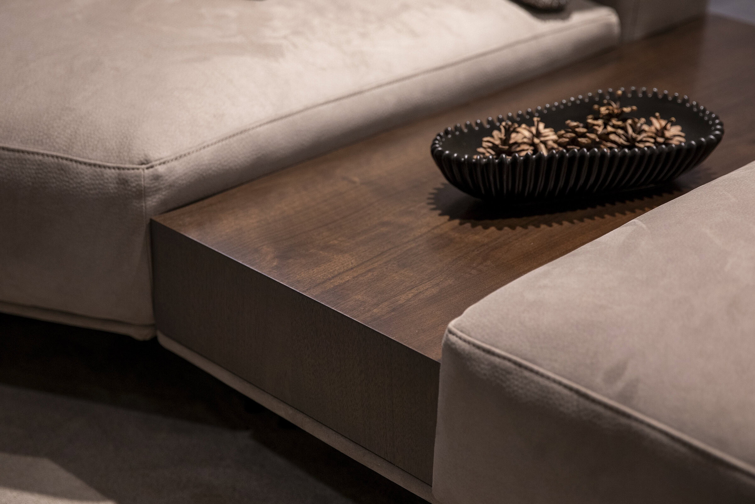 Sleek wooden coffee table with a decorative black bowl filled with pinecones between plush beige sofas in modern living room setting.
