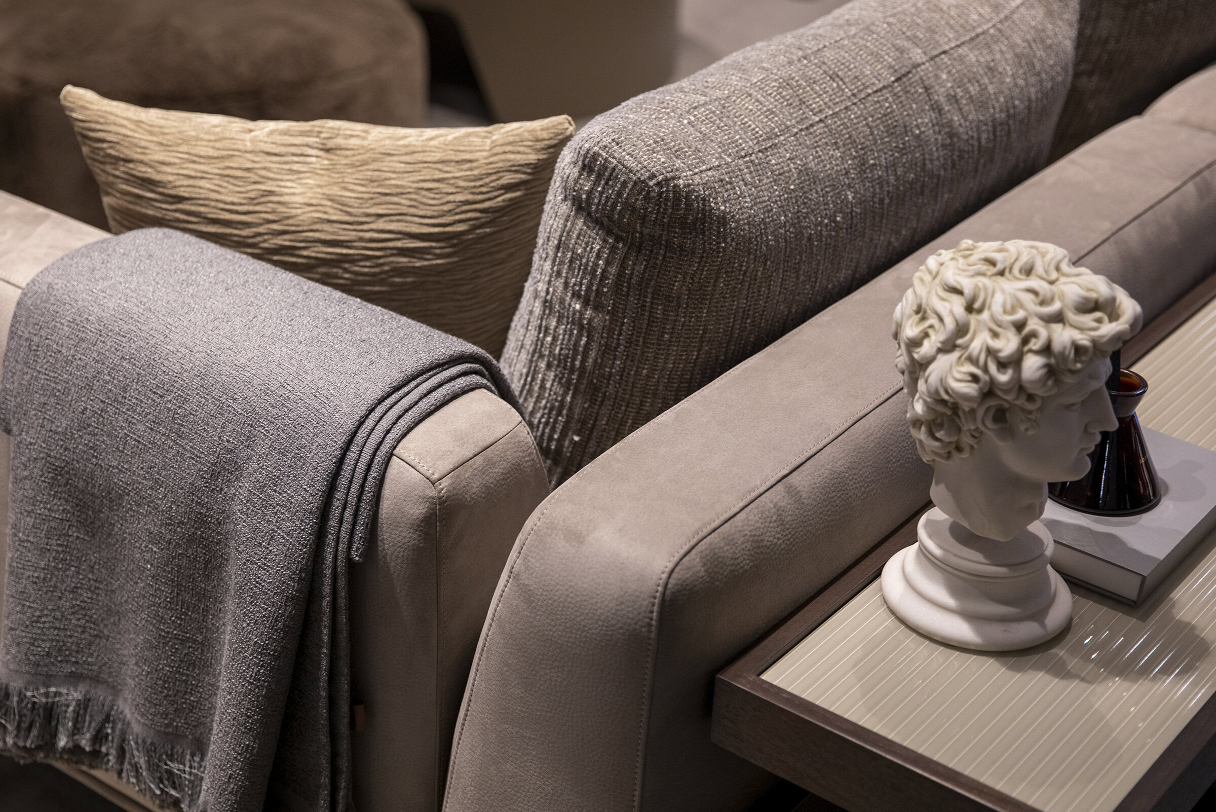 Luxurious beige sofa with textured cushions, a cozy gray throw blanket, and stylish decorative items on a matching side table, showcasing elegant home furniture designs at Saloni Furniture.
