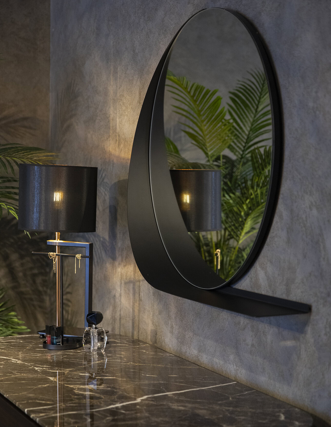 Sleek black modern wall mirror with a crescent moon design, hanging above a marble surface with elegant black table lamps and lush green plants, perfect for contemporary home decor.