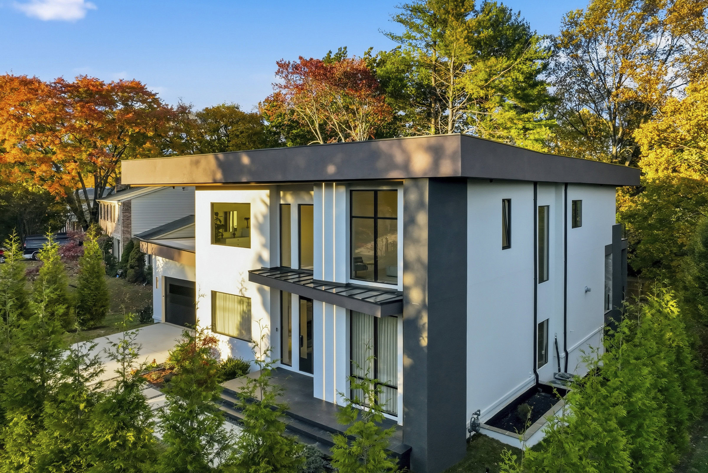 Elegant house featuring modern architecture, clean lines, and expansive windows in a lush green environment during fall.