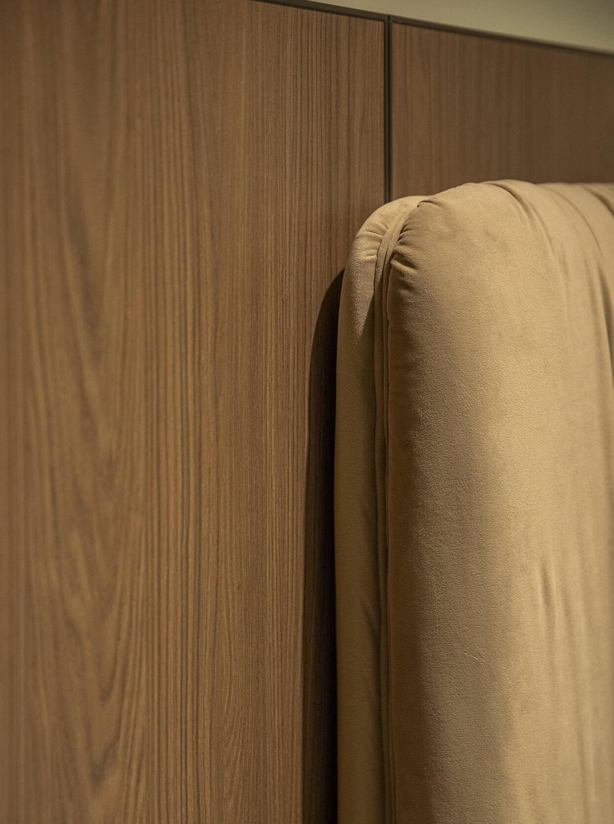 Smooth beige upholstered headboard next to wooden wall paneling in modern bedroom furniture design.