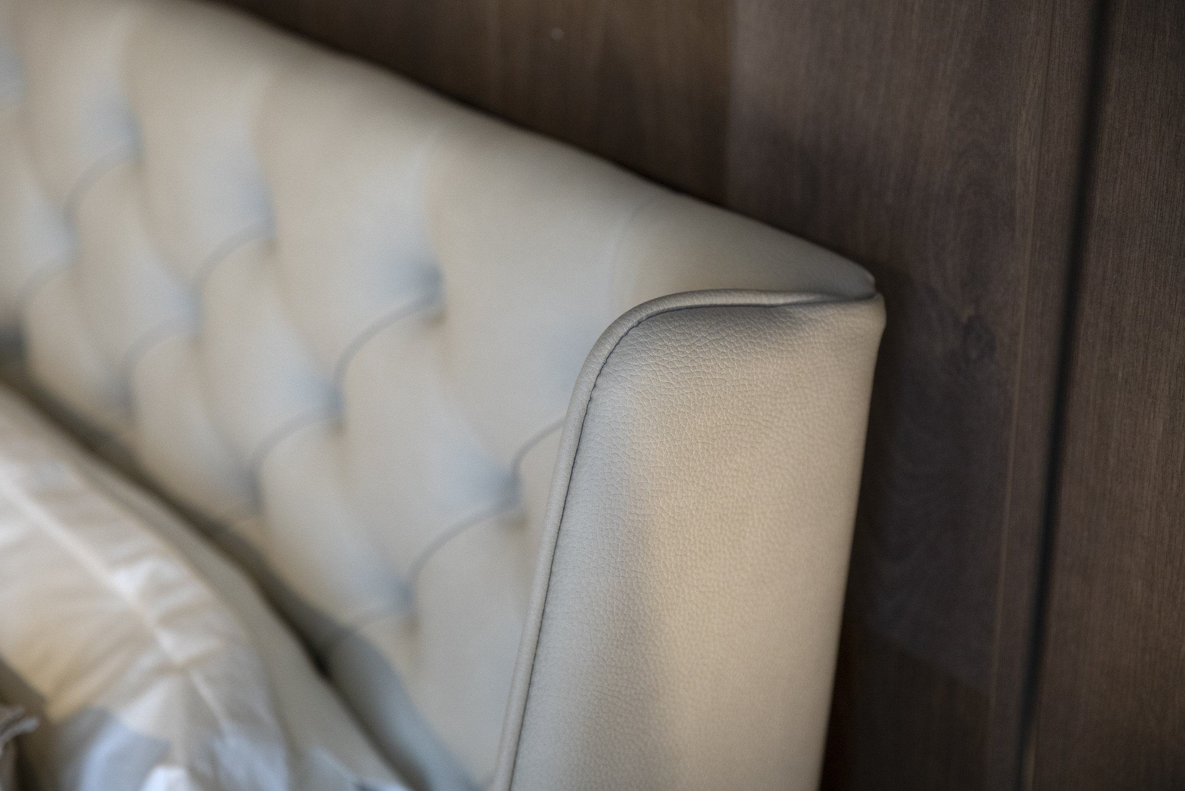 White upholstered bed headboard with tufted design and dark wooden wall background.